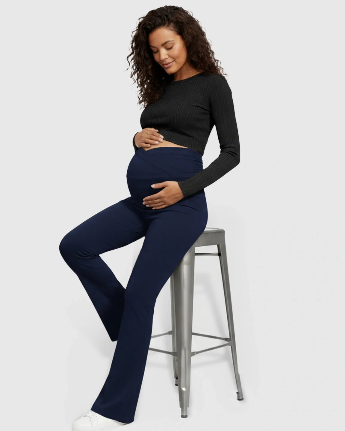 Pregnant woman in navy Bump Society flared maternity pants with a crossed waistband.