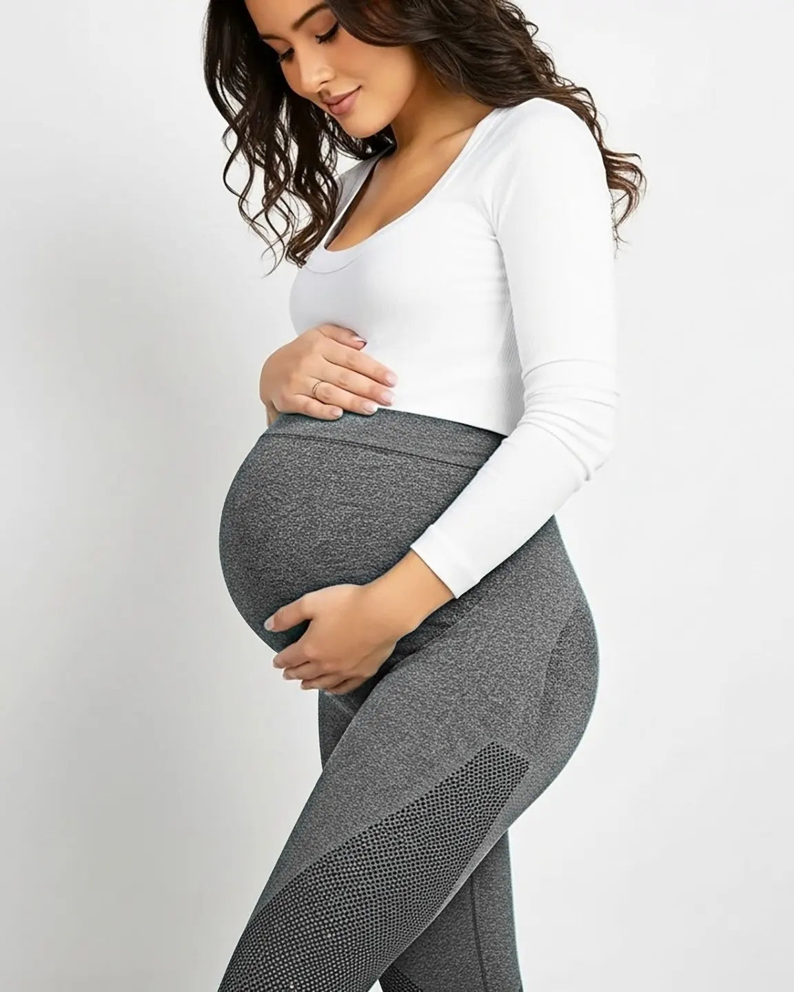 Pregnant woman in gray high-elastic body-hugging maternity leggings with subtle mesh detail and a white top.