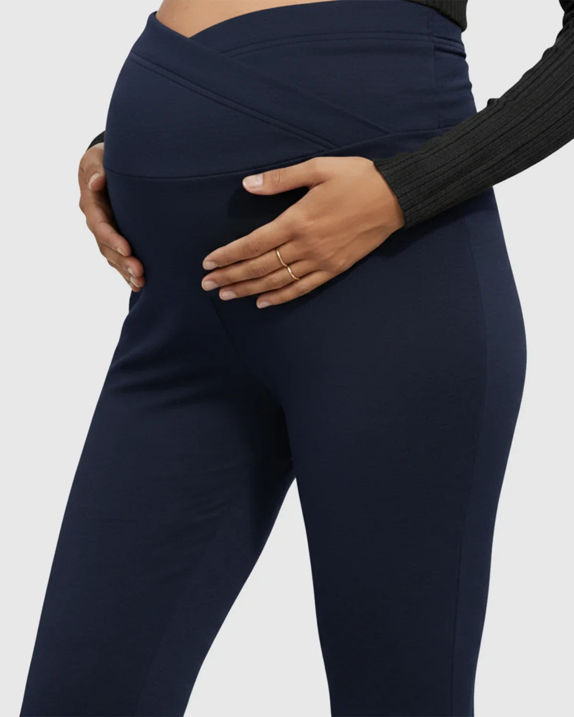 Navy flared maternity pants with a crossed waistband supporting a pregnant belly.