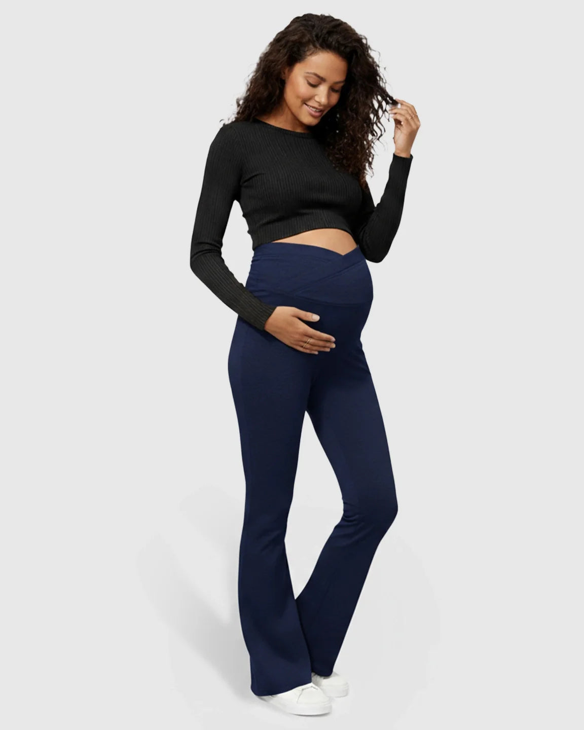 Smiling pregnant woman in navy flared maternity pants with a crossed waistband.