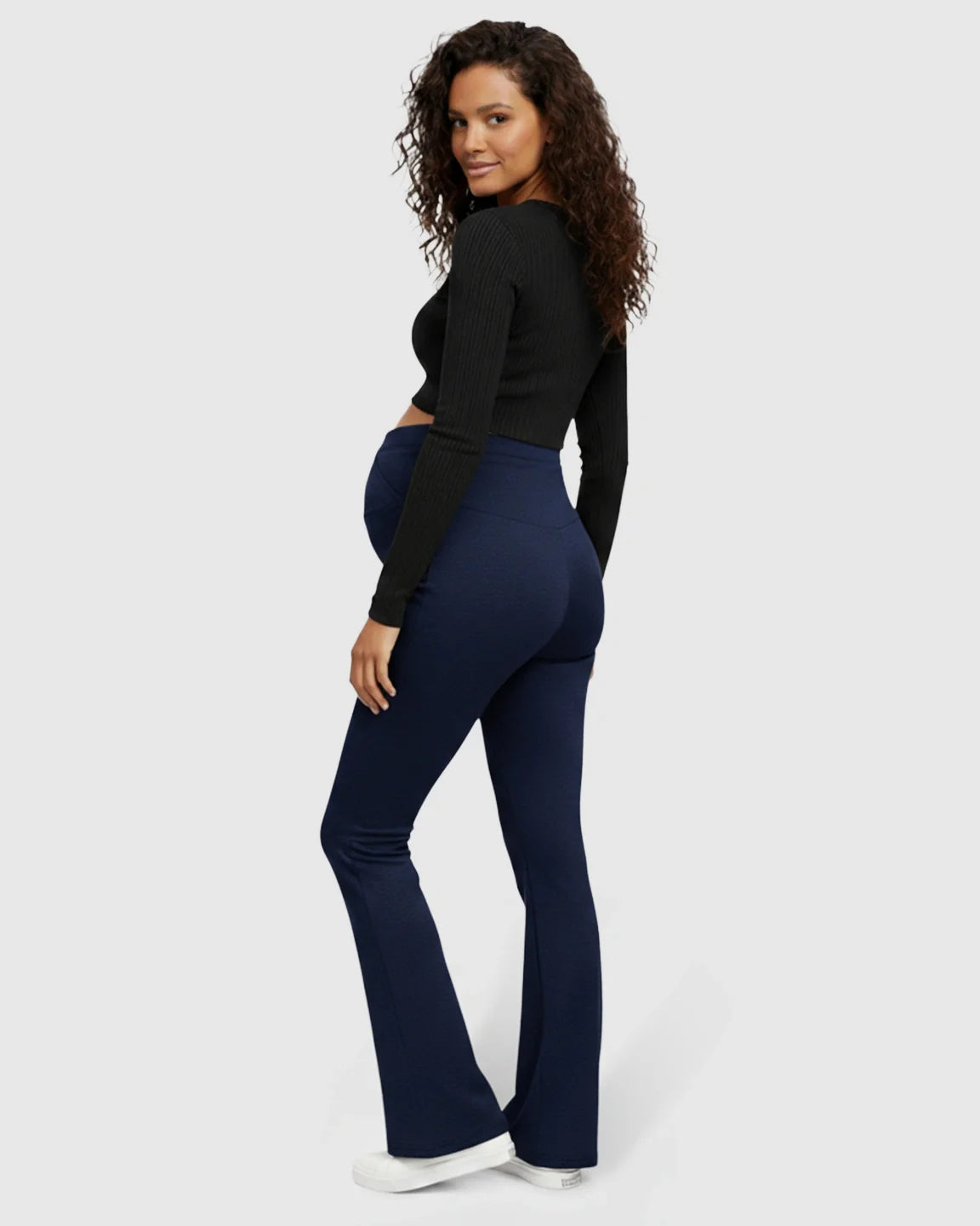 Maternity model in navy flared pants with a crossed waistband, paired with a black crop top.