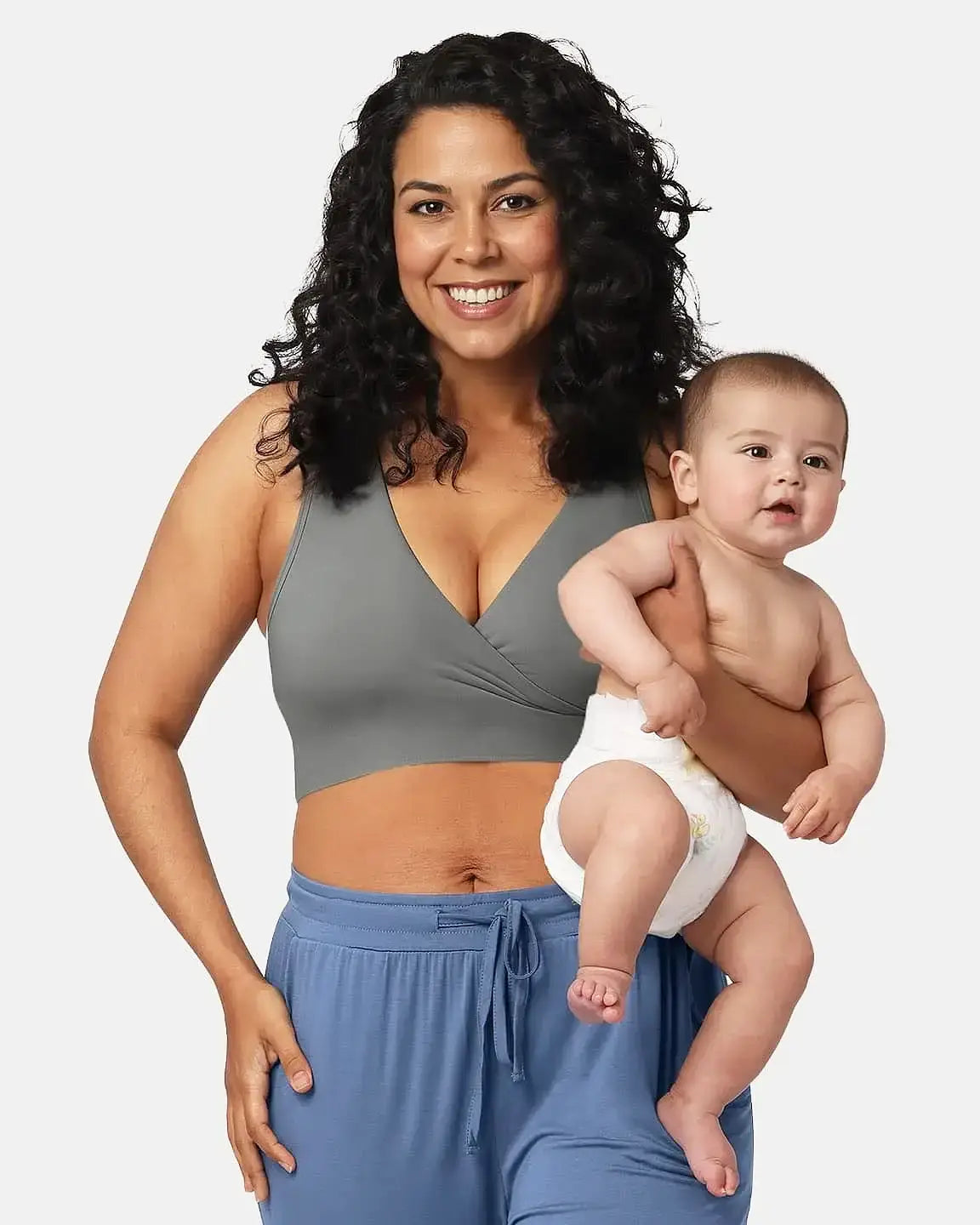 Smiling mom in a gray wire-free nursing bra and blue pants, holding a baby.