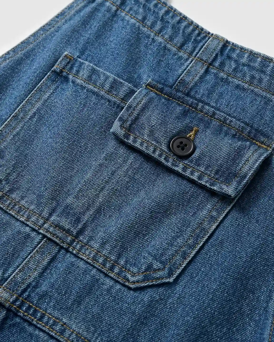Close-up of blue denim maternity overalls with a practical flap pocket and black button.