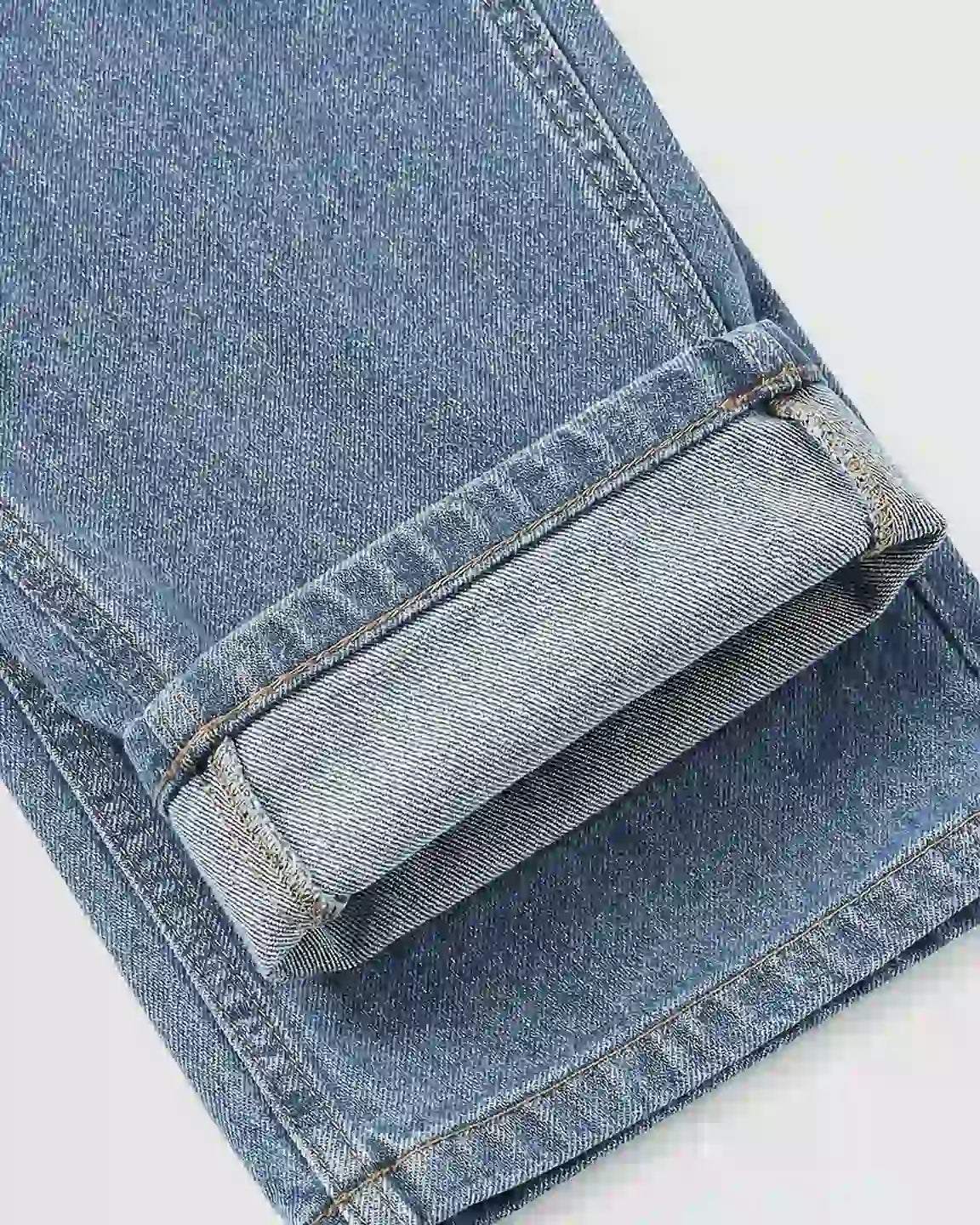 Close-up of a light blue denim maternity jumpsuit leg with a wide, cuffed hem and visible stitching.
