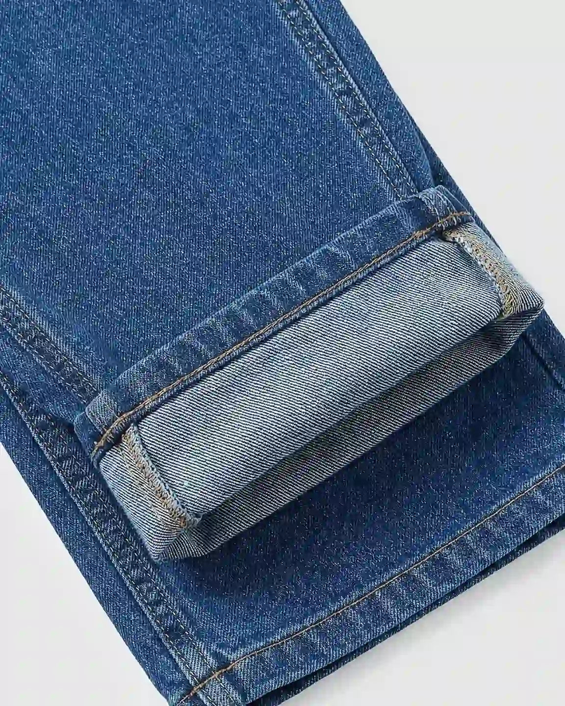 Close-up of a blue denim maternity jumpsuit leg, cuffed at the hem, showing fabric texture and stitching.