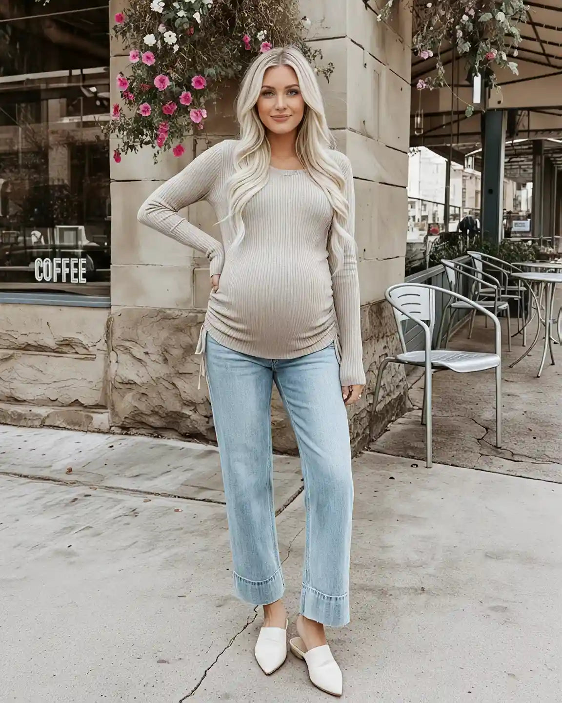 Blonde pregnant woman in a beige ribbed long-sleeve maternity top with adjustable side drawstrings and light wash jeans.