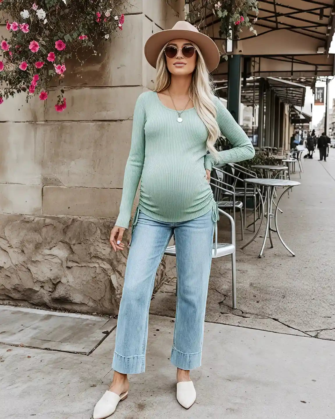 Blonde pregnant woman wearing a mint green ribbed maternity top with adjustable side drawstrings, light wash jeans, and a hat.