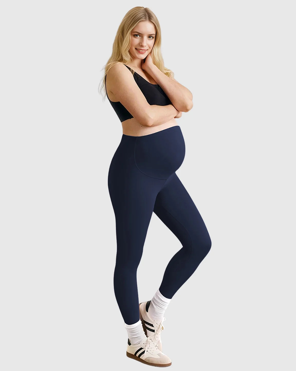 Smiling pregnant woman in navy high-waist sculpting maternity leggings and a black bra.
