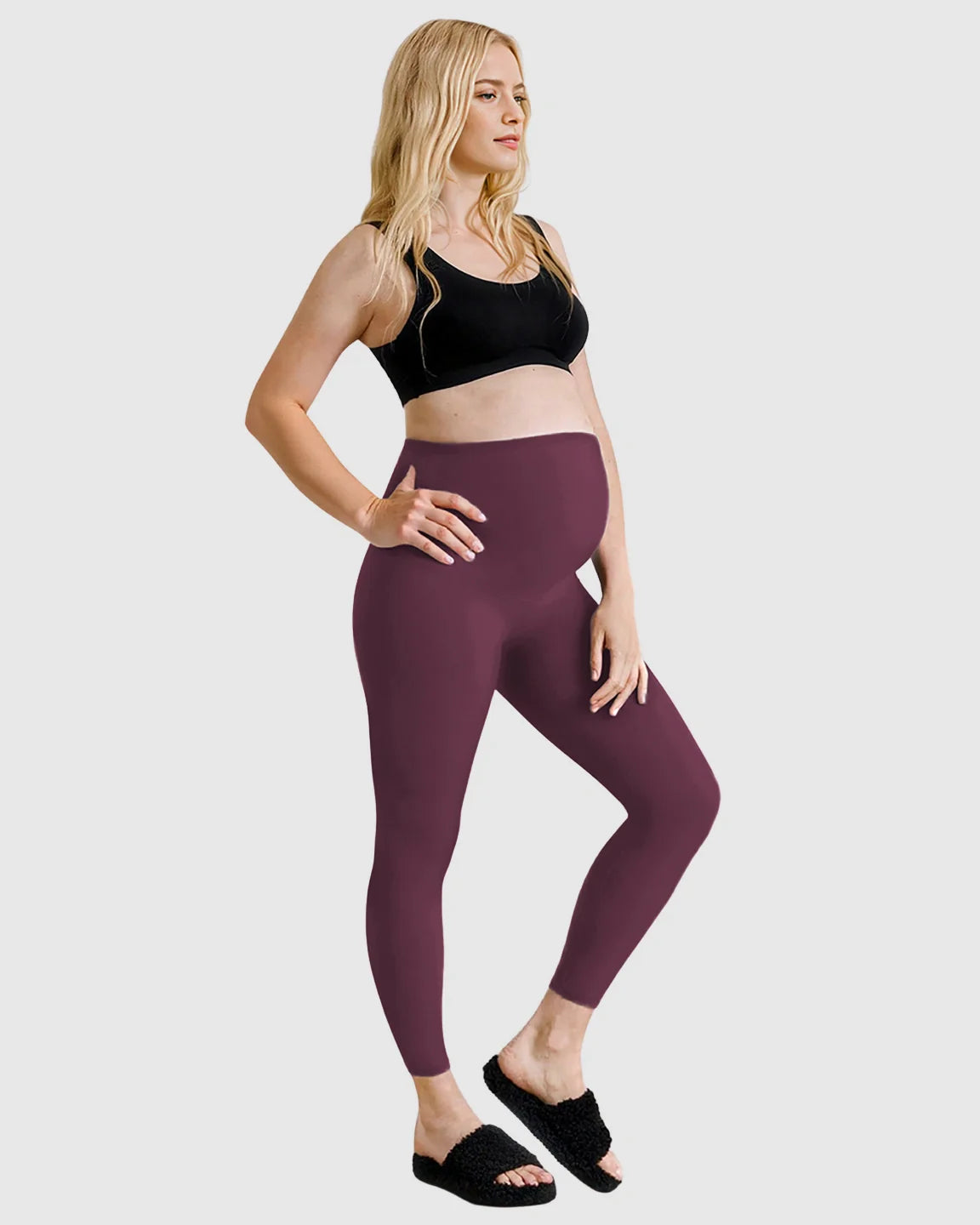 Blonde pregnant woman wearing high-waist plum sculpting maternity leggings and a black sports bra.