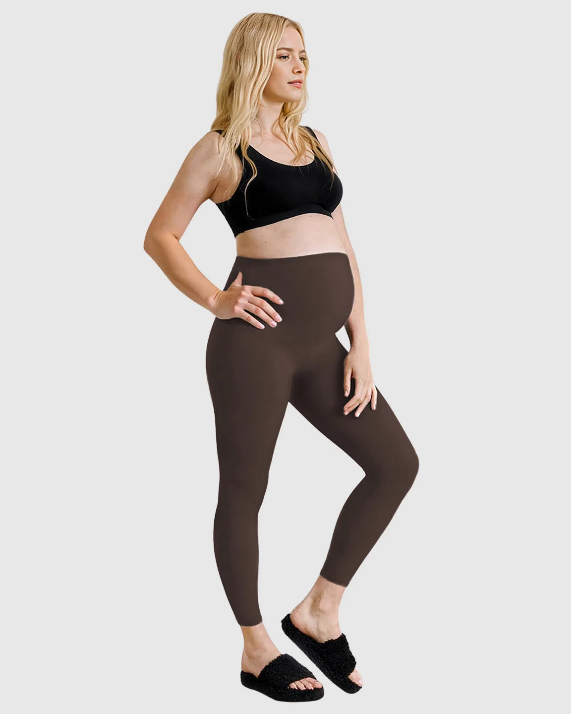 Blonde pregnant woman wearing dark brown high-waist sculpting maternity leggings and a black bra.