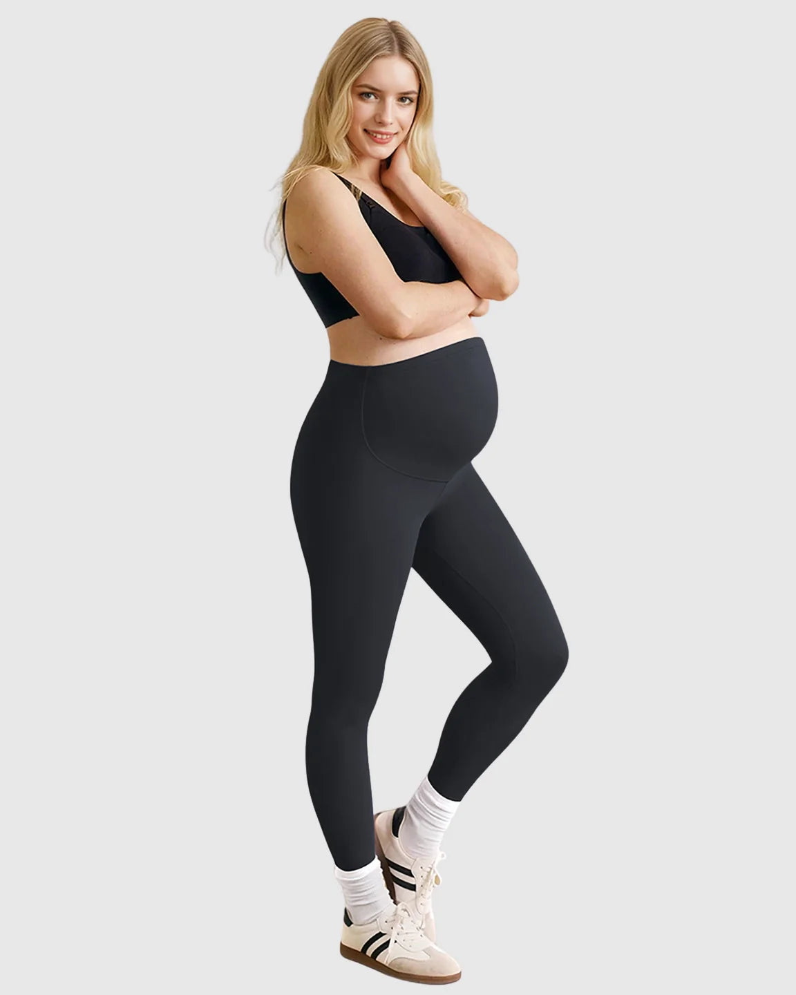 Smiling pregnant woman in black high-waist sculpting maternity leggings and a black bra.