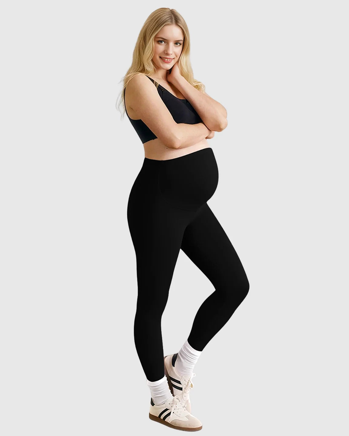 Smiling pregnant woman wearing black high-waist sculpting maternity leggings and a black bra.