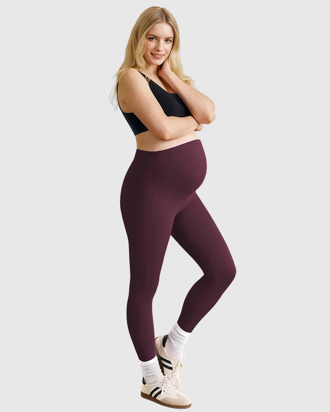 Smiling pregnant woman in dark plum high-waist sculpting maternity leggings and a black bra.