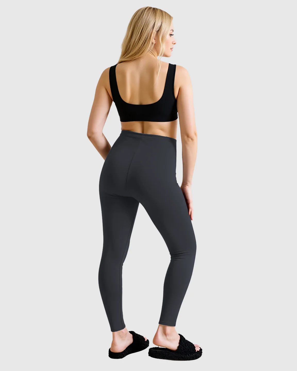 Blonde woman from behind wearing dark gray high-waist sculpting maternity leggings and a black sports bra.
