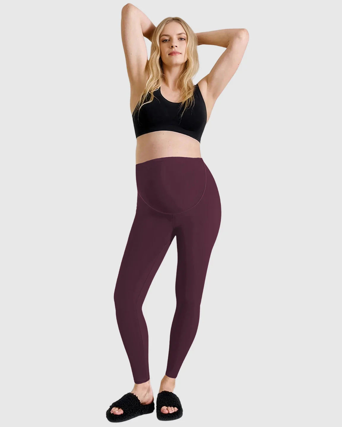 Blonde woman in black sports bra and plum high-waist sculpting maternity leggings with belly support.