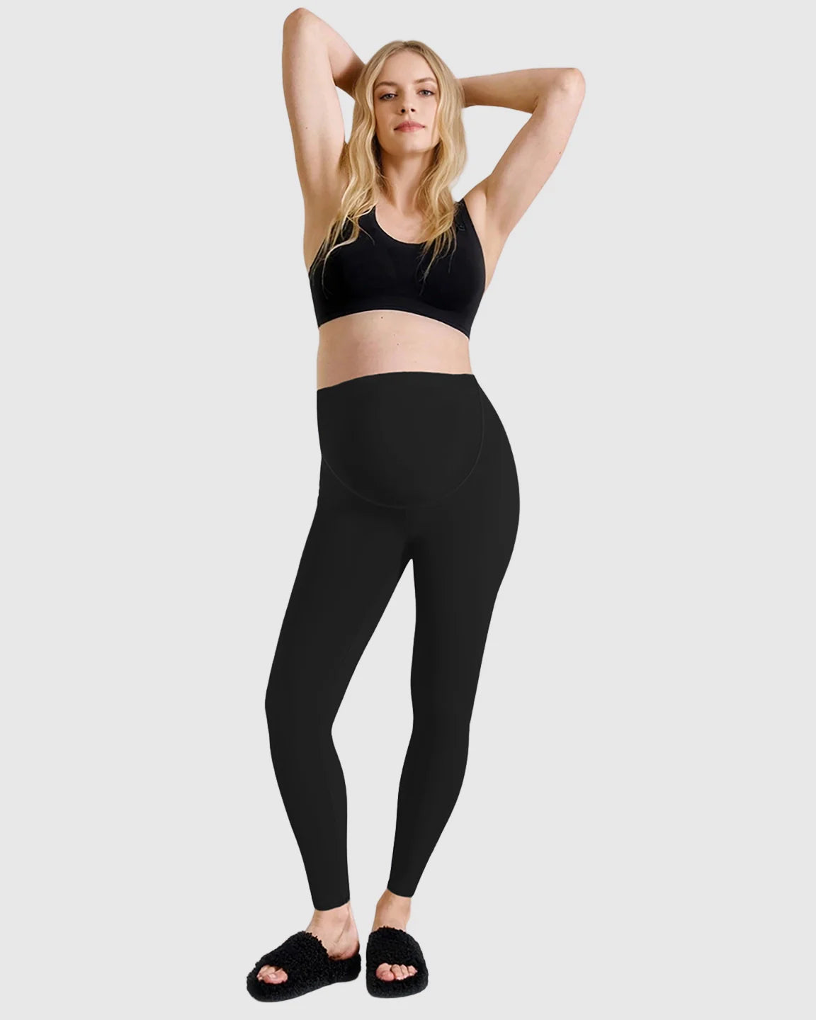 Pregnant woman in black high-waist sculpting maternity leggings and a black sports bra.