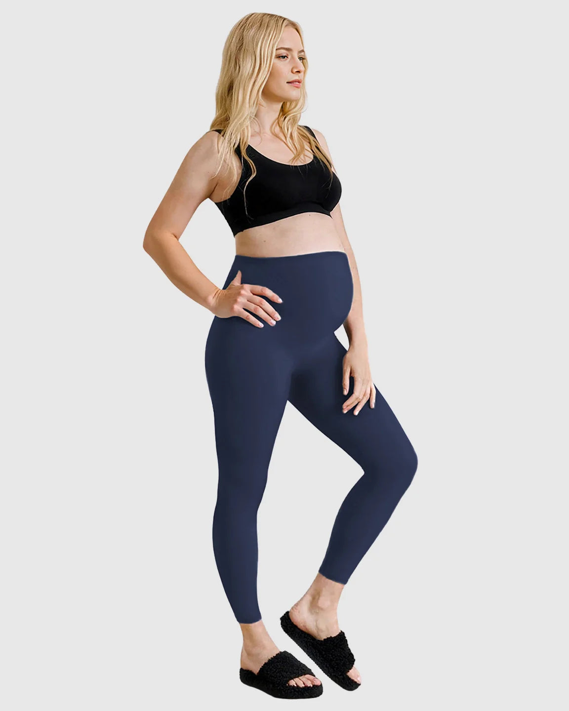Blonde pregnant woman wearing navy high-waist sculpting maternity leggings and a black bra.