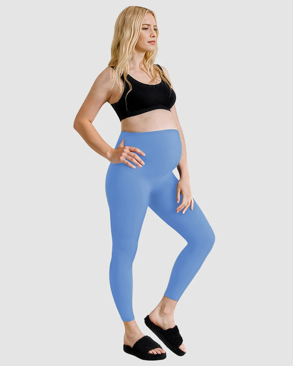 Blonde pregnant woman wearing high-waist, seamless blue maternity leggings and a black sports bra.