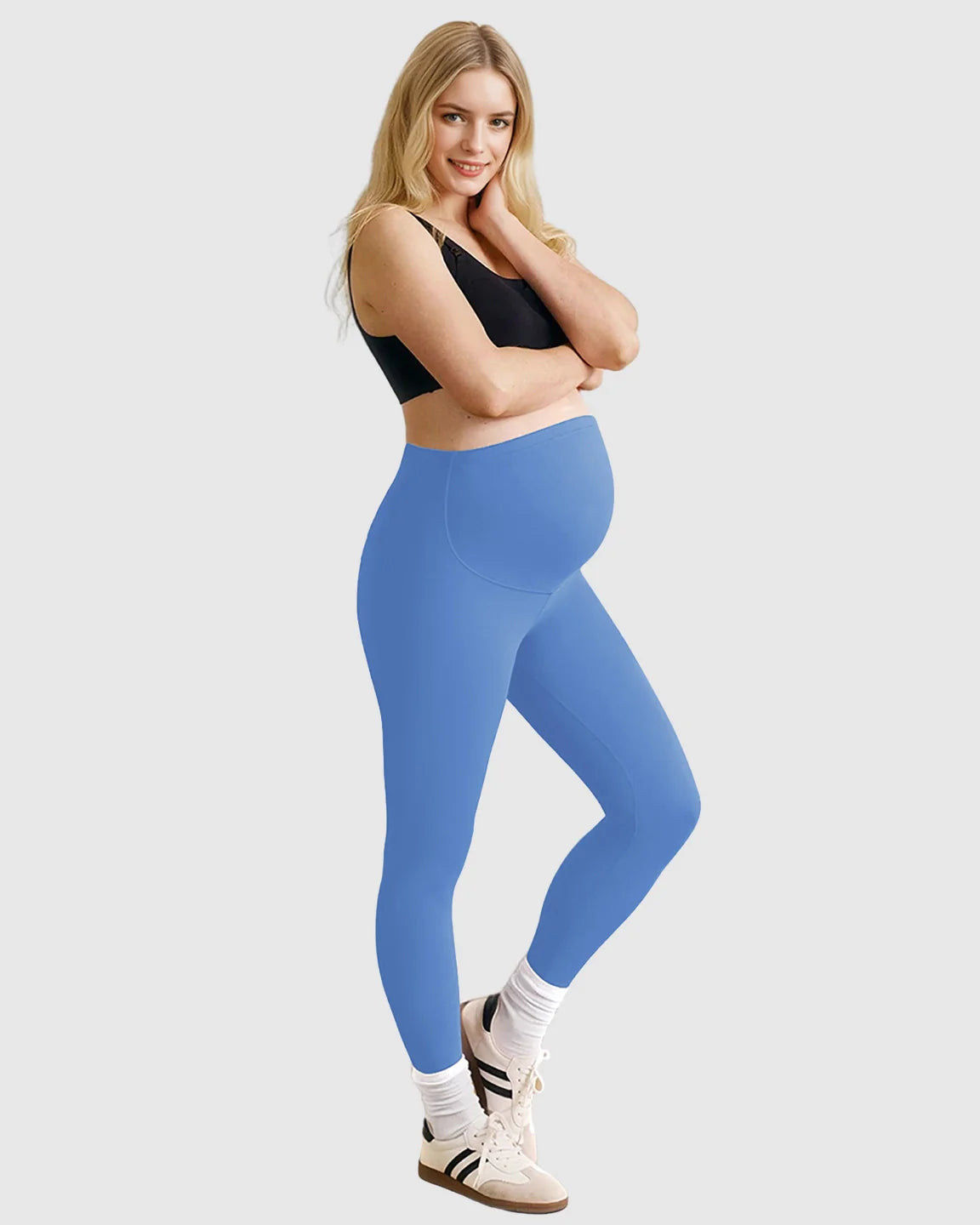 Smiling pregnant woman in blue high-waist sculpting maternity leggings and a black bra.