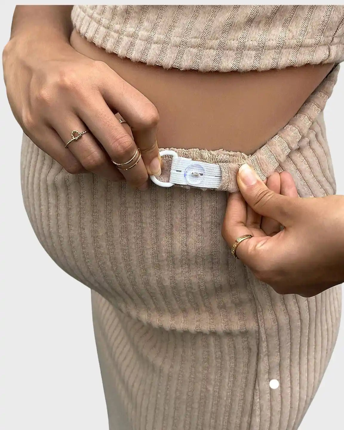 Pregnant woman adjusting the elastic waistband of a beige ribbed maternity midi skirt with a side slit.