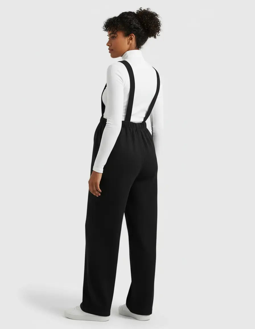 Woman wearing a black corduroy maternity jumpsuit with adjustable straps over a white long-sleeve top.
