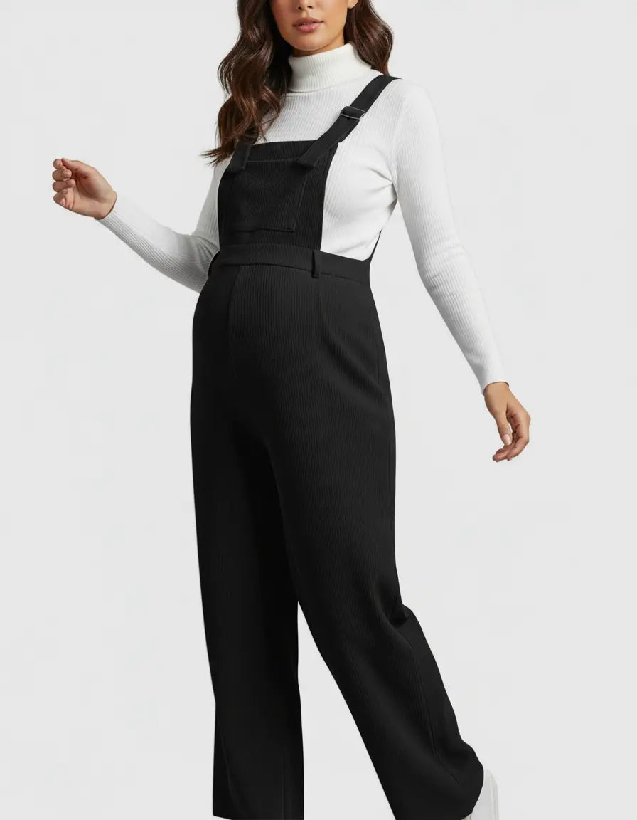 Pregnant woman in black corduroy maternity jumpsuit with adjustable straps over a white turtleneck.