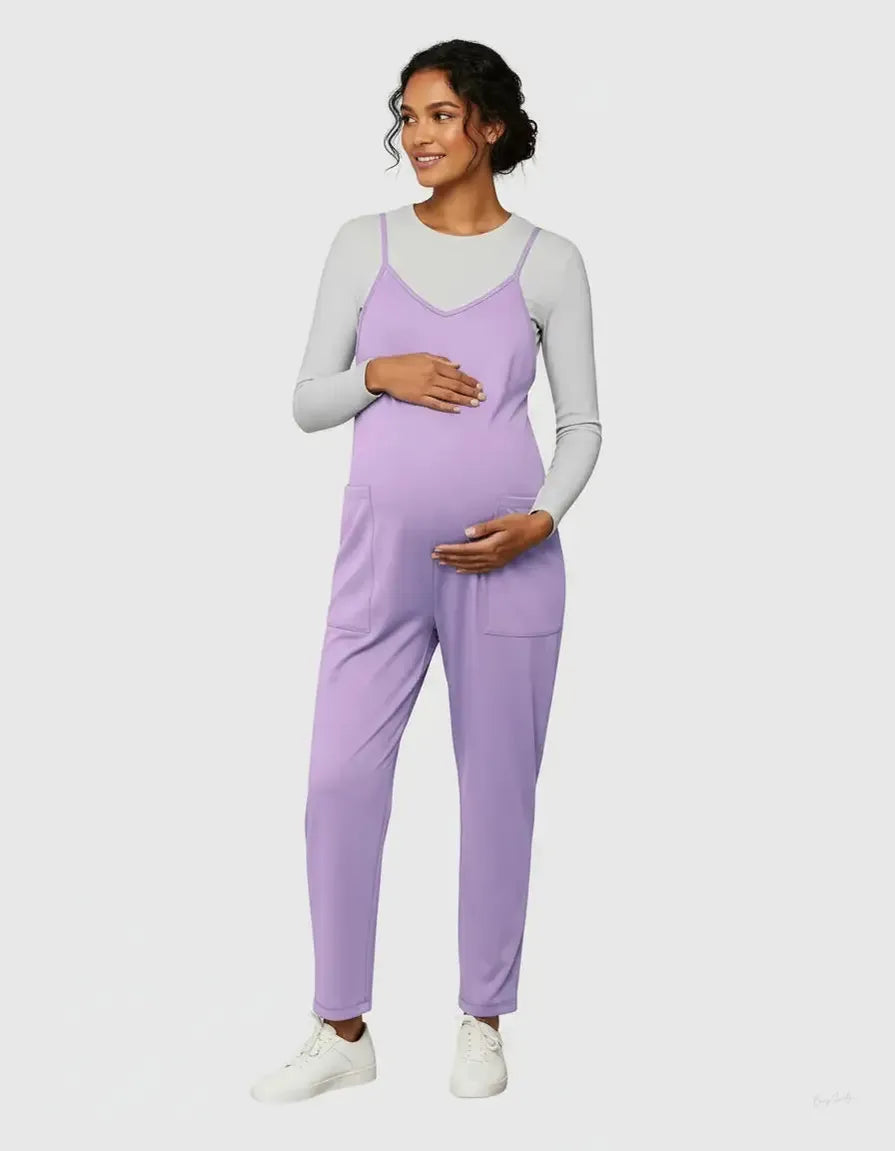 Smiling pregnant woman in a lavender flowy maternity jumpsuit with adjustable straps and front pockets.