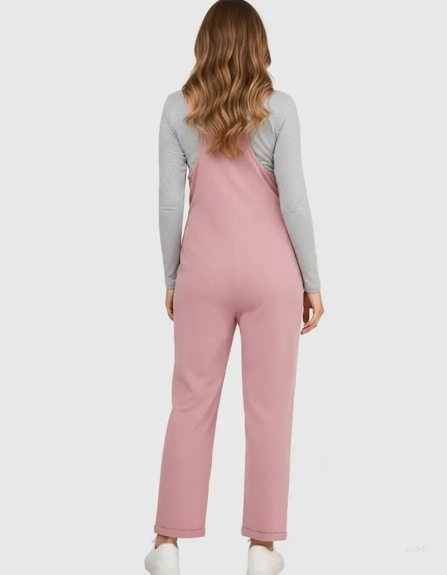 Woman from behind in a pink flowy maternity jumpsuit with adjustable straps over a gray long-sleeve shirt.