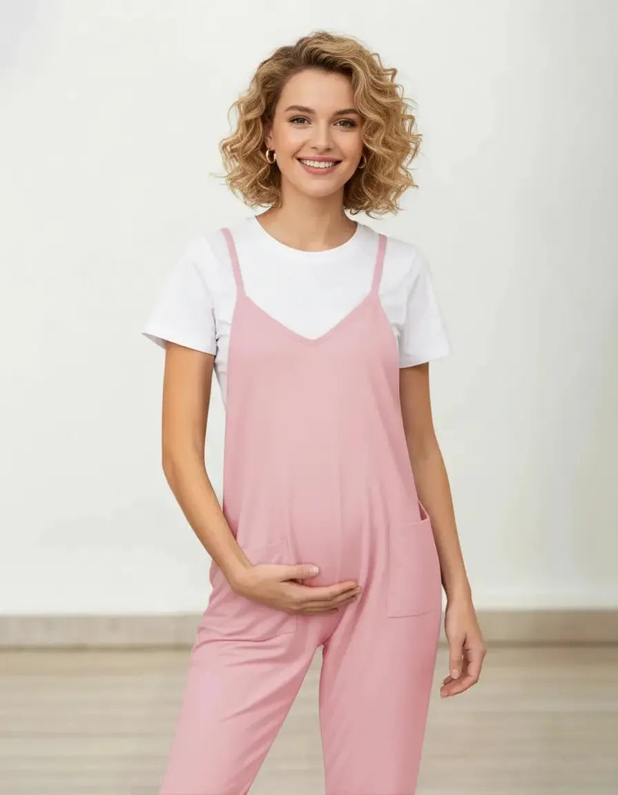 Smiling pregnant woman in a pink flowy maternity jumpsuit with adjustable straps and pockets, over a white tee.