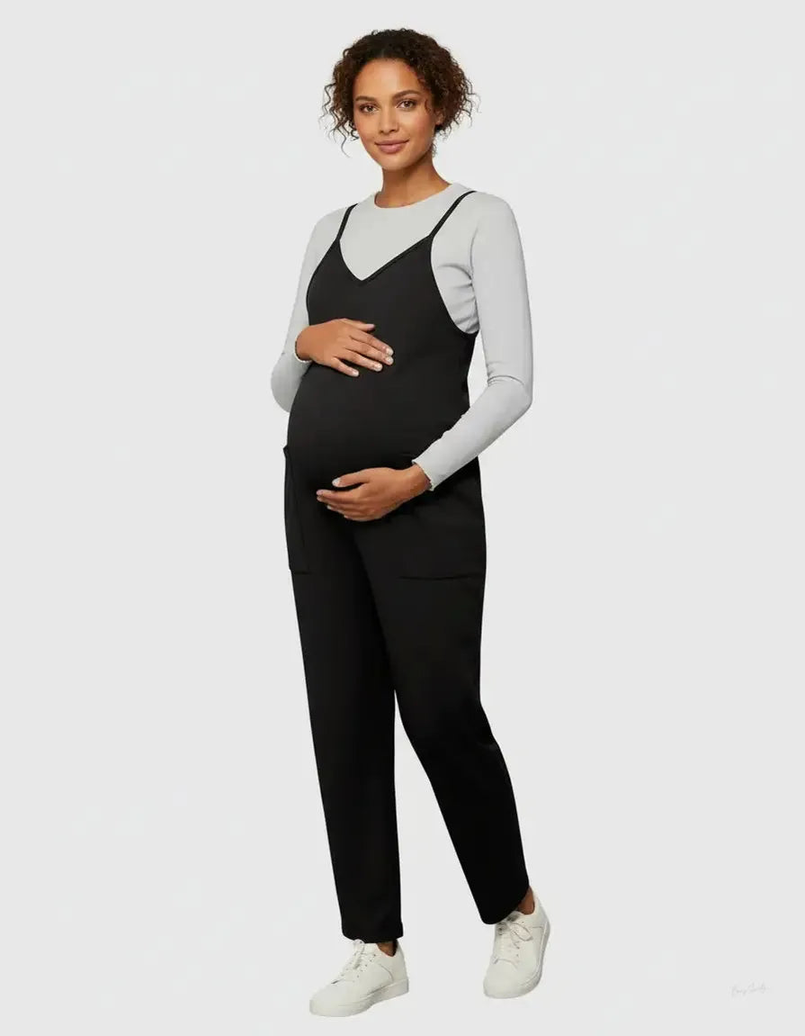 Pregnant woman in a black flowy maternity jumpsuit with adjustable straps over a light grey long-sleeve top.