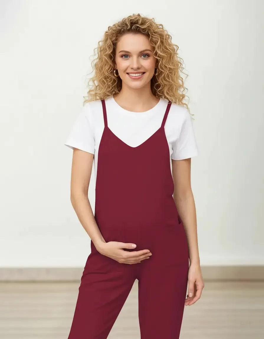 Smiling pregnant woman in a flowy, adjustable strap burgundy maternity jumpsuit over a white tee.