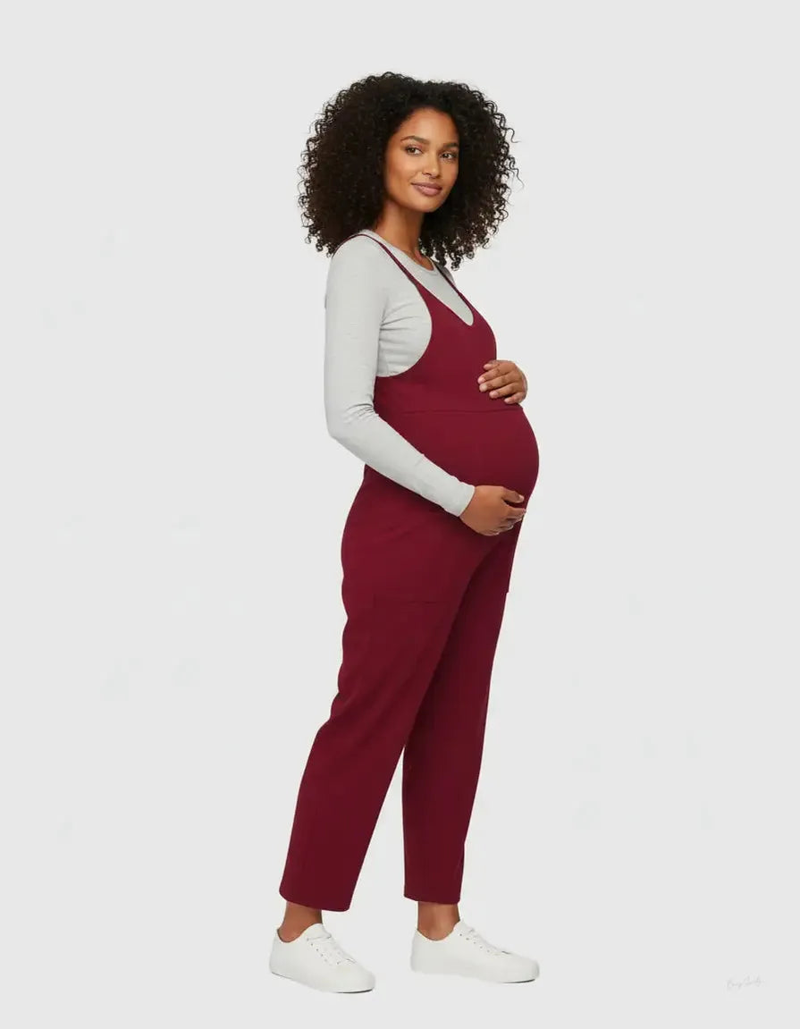 Pregnant woman in a flowy, dark red maternity jumpsuit with adjustable straps and side pockets.