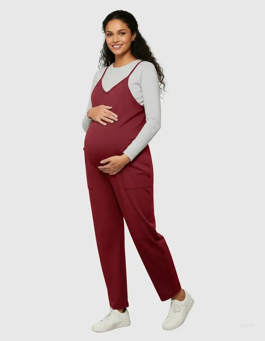 Smiling pregnant woman in a flowy, red maternity jumpsuit with adjustable straps and pockets.