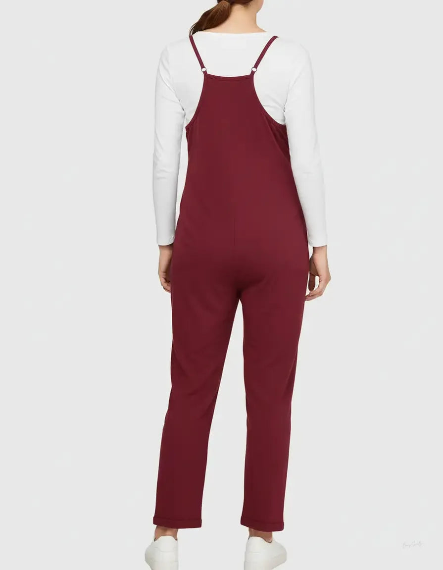 Woman from behind wearing a flowy, adjustable strap burgundy maternity jumpsuit over a white long-sleeve top.