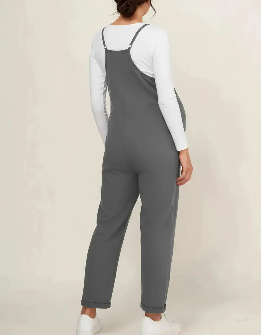 Maternity jumpsuit in charcoal gray with adjustable straps, worn over a white long-sleeve top.