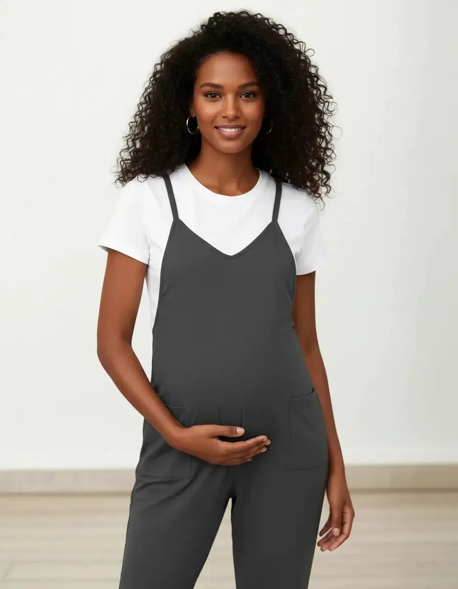 Smiling pregnant woman in a dark gray maternity jumpsuit with adjustable straps over a white t-shirt.