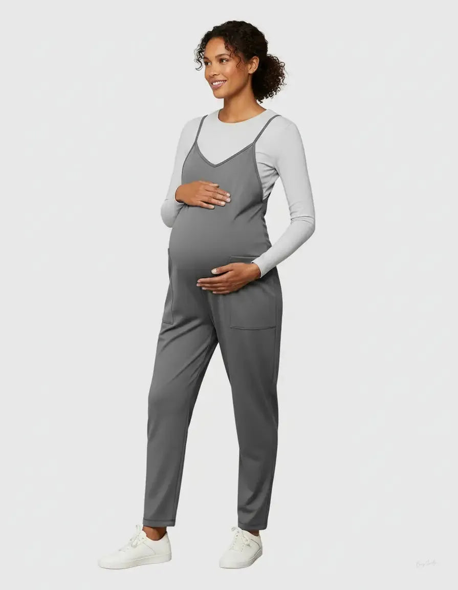 Pregnant woman in a gray flowy maternity jumpsuit with adjustable straps and pockets, layered over a white long-sleeve top.