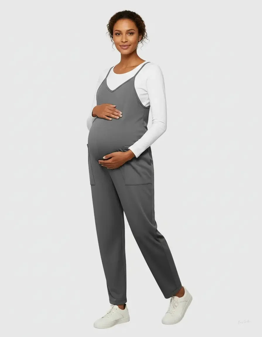 Pregnant woman in a gray flowy maternity jumpsuit with adjustable straps, pockets, and a white long-sleeve shirt.