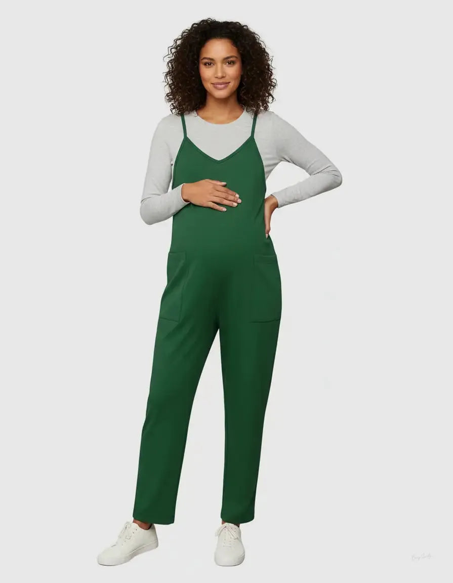Pregnant woman in a green flowy maternity jumpsuit with adjustable straps over a grey long-sleeve top.