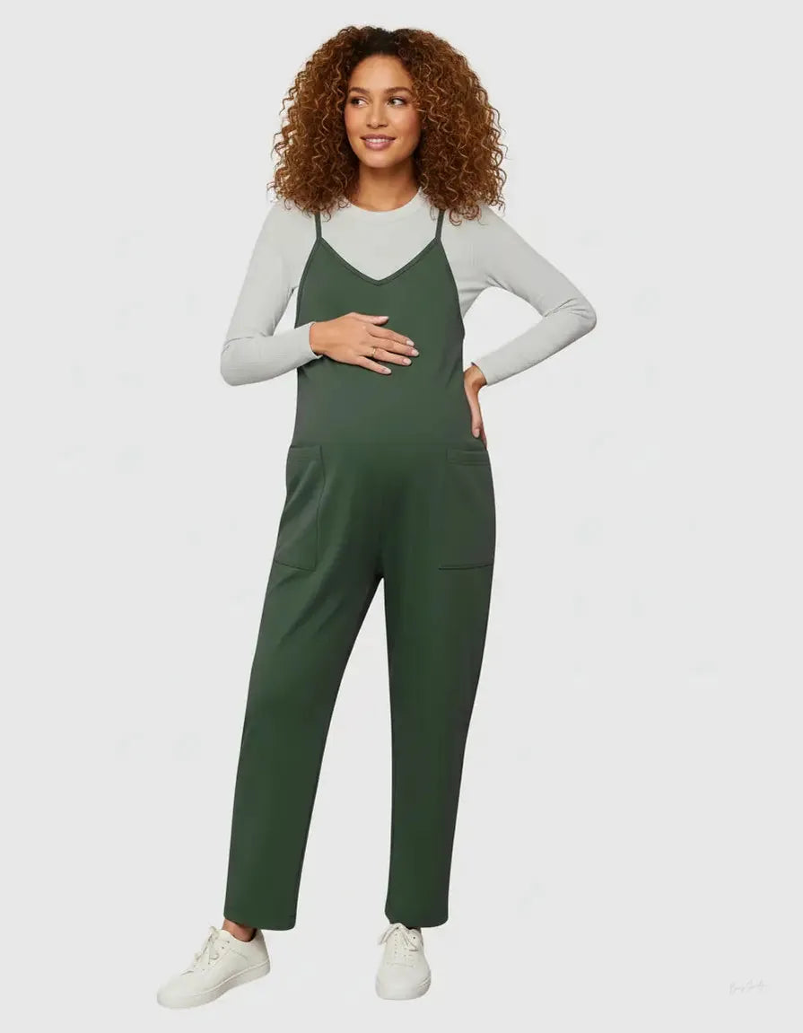 Maternity model in a dark green flowy jumpsuit with adjustable straps, worn over a light gray long-sleeve top.