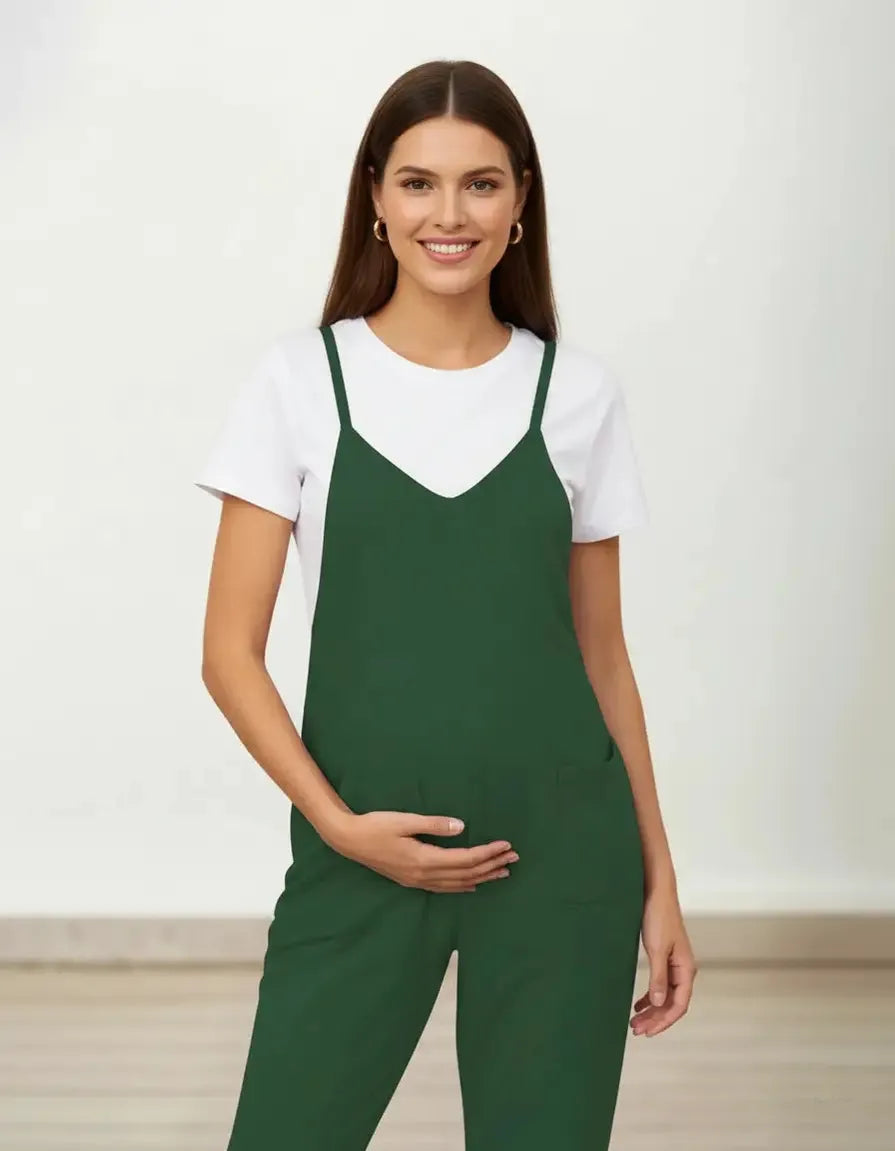 Smiling pregnant woman in a dark green flowy maternity jumpsuit with adjustable straps and pockets.