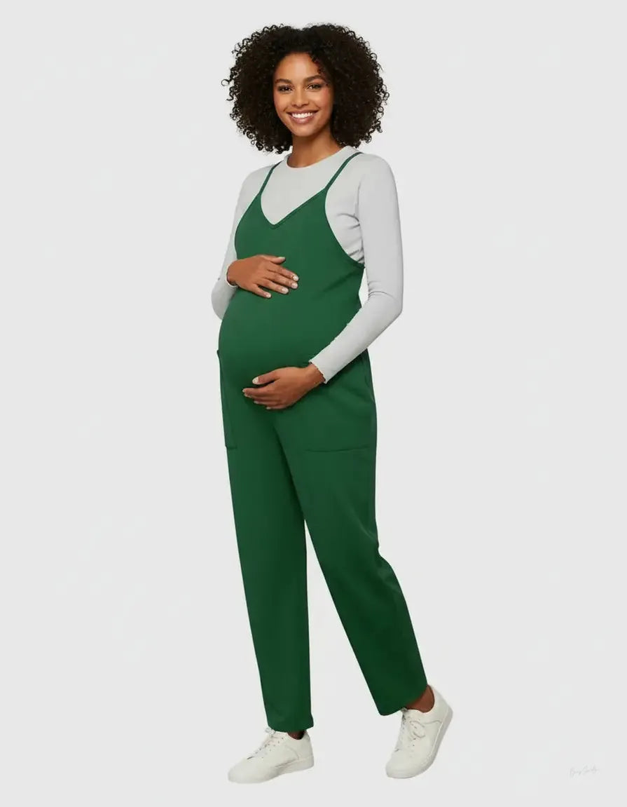 Smiling pregnant woman in a dark green adjustable strap flowy maternity jumpsuit with pockets, layered over a white long-sleeve top.