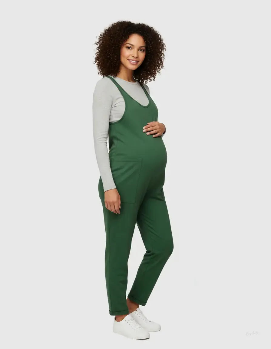Smiling pregnant woman in a green flowy maternity jumpsuit with adjustable straps and pockets.