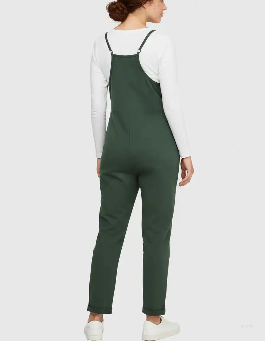 Woman in a dark green flowy maternity jumpsuit with adjustable straps over a white long-sleeve top.