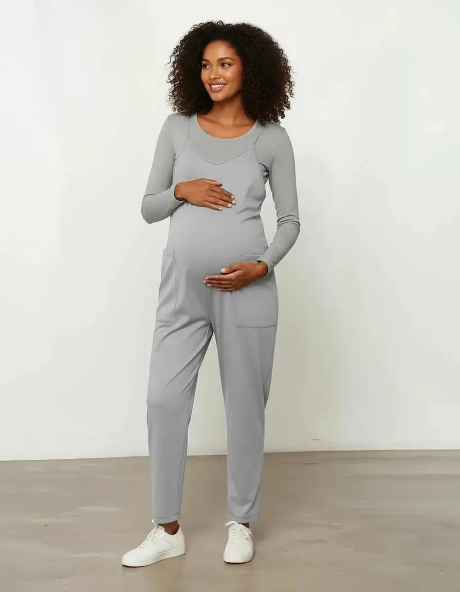 Smiling pregnant woman in a gray flowy maternity jumpsuit with adjustable straps and pockets.