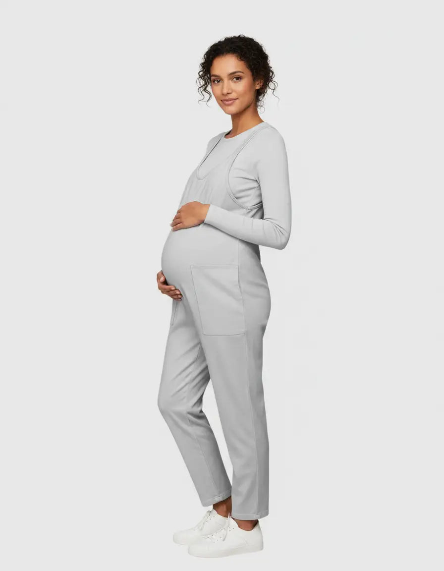 Pregnant woman in a light grey flowy maternity jumpsuit with adjustable straps and front pockets.