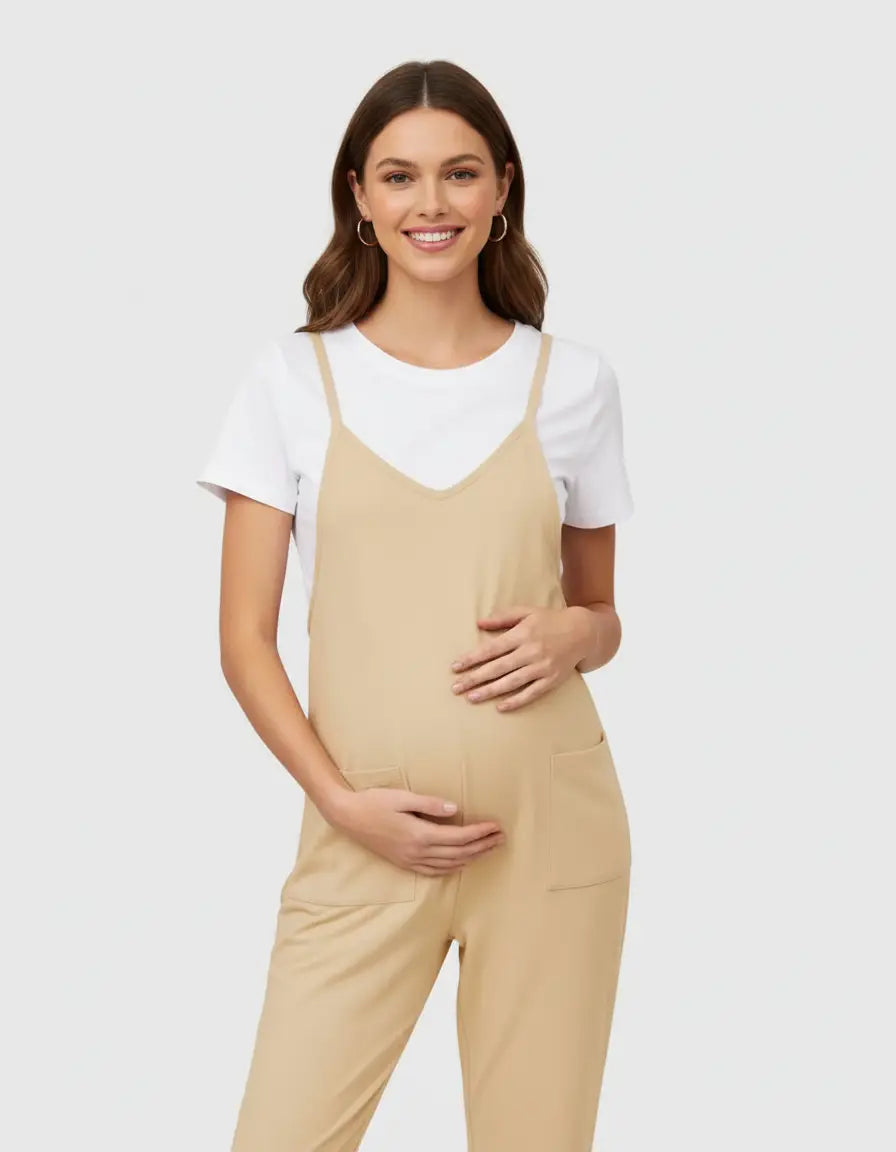 Smiling pregnant woman in a beige flowy maternity jumpsuit with adjustable straps and pockets, over a white tee.