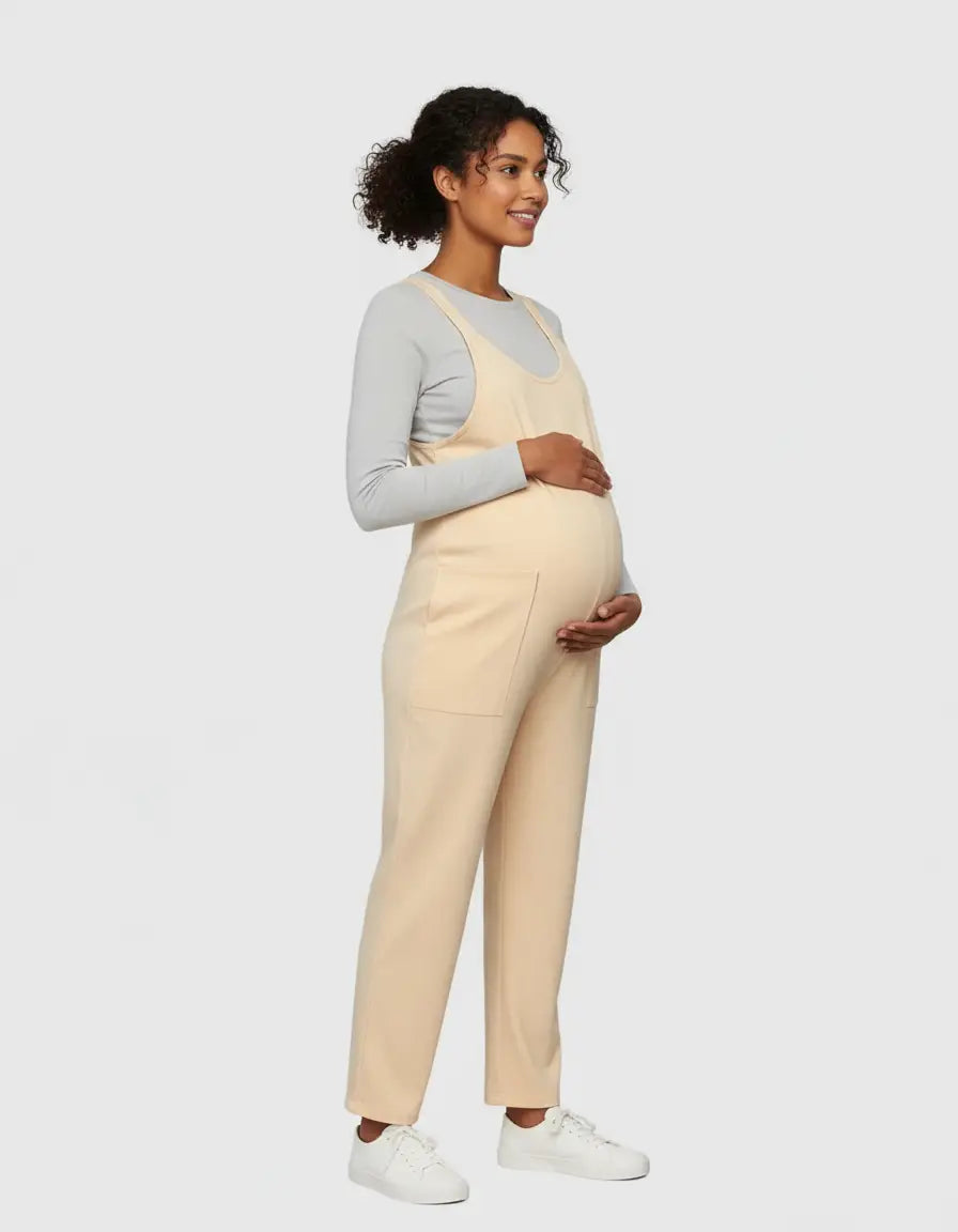 Pregnant woman in a beige flowy maternity jumpsuit with adjustable straps and front pockets.