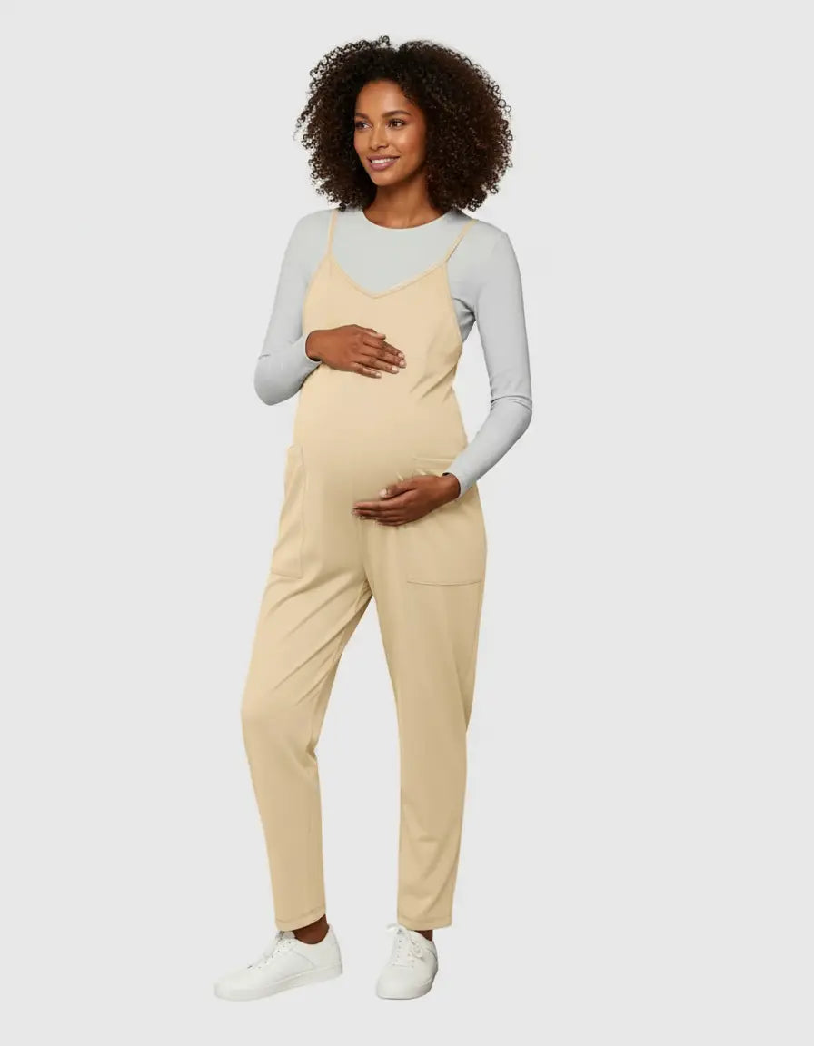 Pregnant woman in a flowy, beige maternity jumpsuit with adjustable straps over a grey long-sleeve shirt.