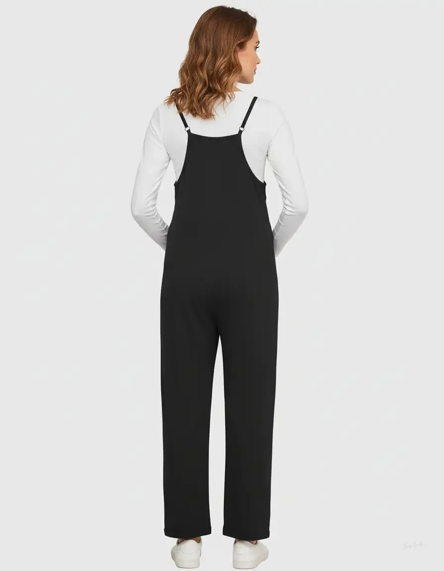 Black flowy maternity jumpsuit with adjustable straps over a white long-sleeve shirt.